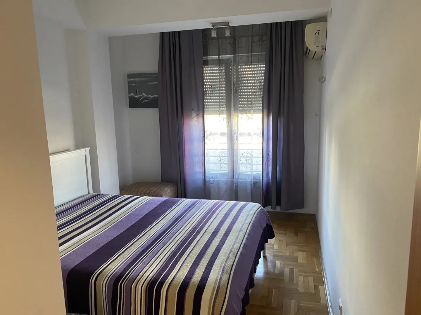 Bright bedroom featuring a striped bedspread and a large window.