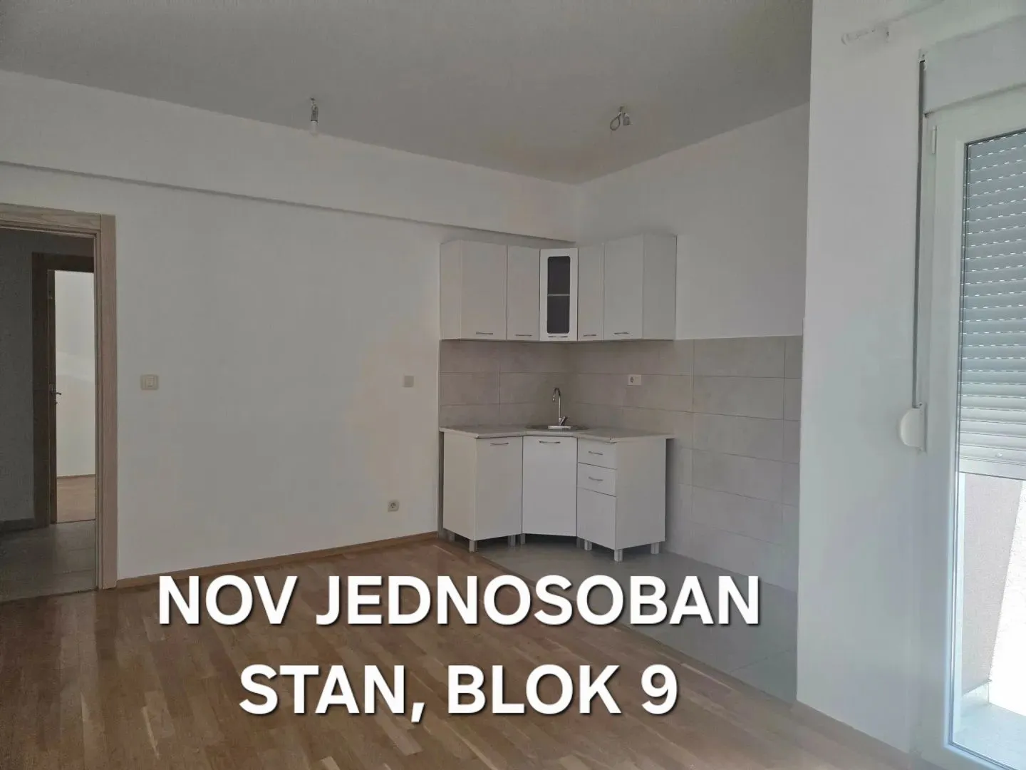 Small white kitchen integrated into the living area with laminate flooring.