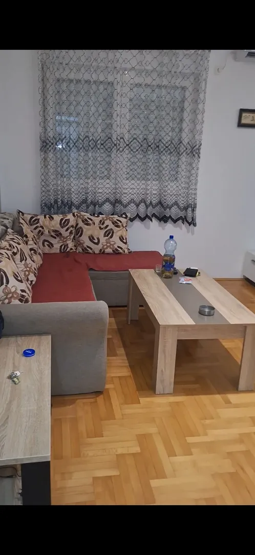 Dnevna soba sa ugaonom garniturom, stočićem i parketom na podu.