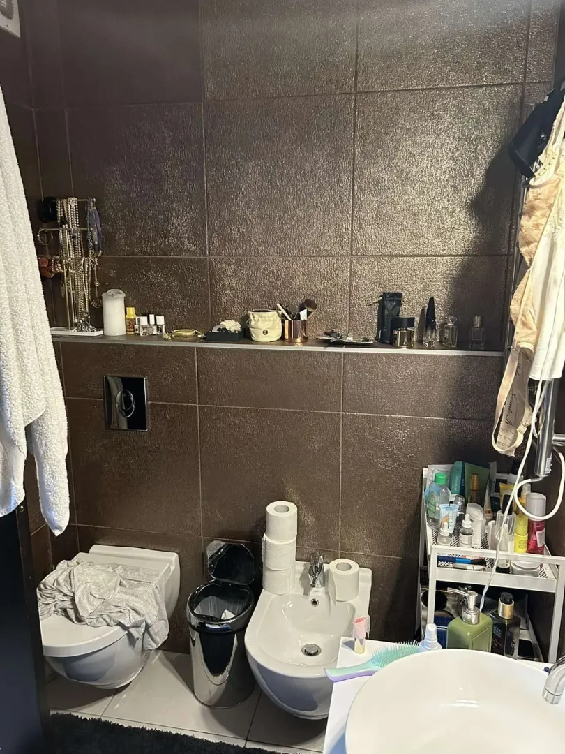Kupatilo sa tamnim pločicama i sanitarijama.