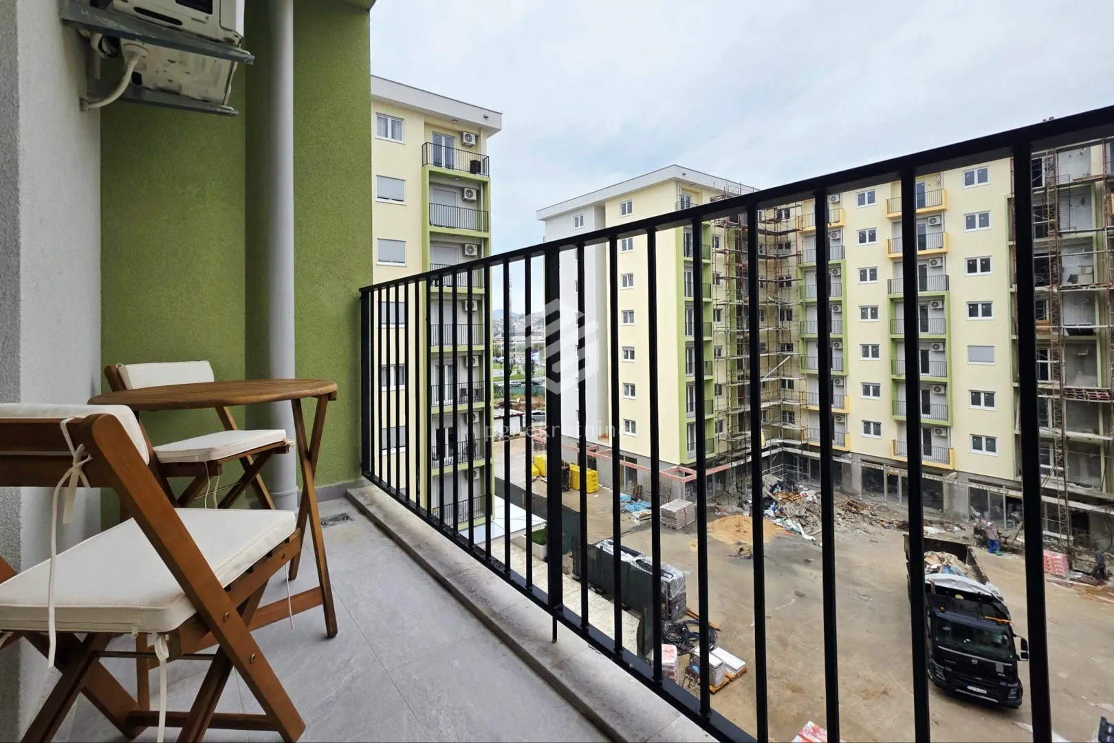 Small balcony with a wooden table and chairs and a view of surrounding buildings under construction.