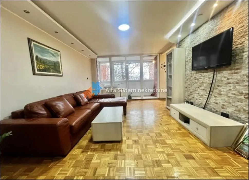 Dnevna soba sa kožnom garniturom, TV-om i parketom na podu.