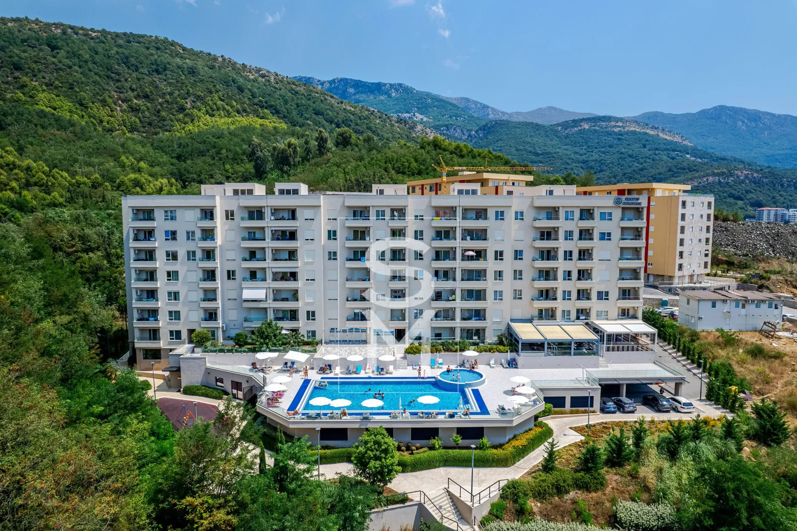 Aerial view of a residential complex with a swimming pool at the foot of the mountain.