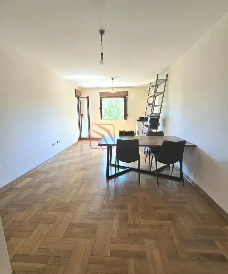 Prazna soba sa parketom na podu i trpezarijskim stolom sa stolicama.
