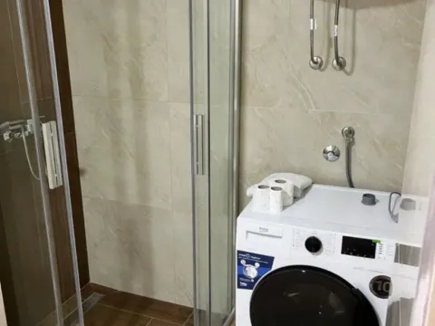 Small bathroom with a shower cabin, washing machine, and water heater. - image 3