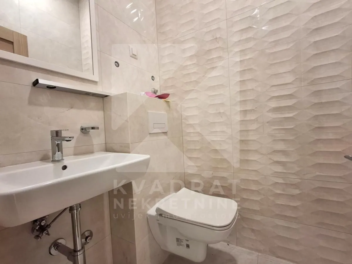 Smaller bathroom lined with ceramic tiles featuring a washbasin and a wall-hung toilet.
