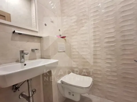Smaller bathroom lined with ceramic tiles featuring a washbasin and a wall-hung toilet. - image 4