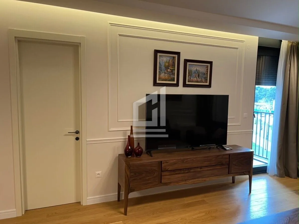 Dnevna soba sa drvenom komodom, televizorom i vratima.