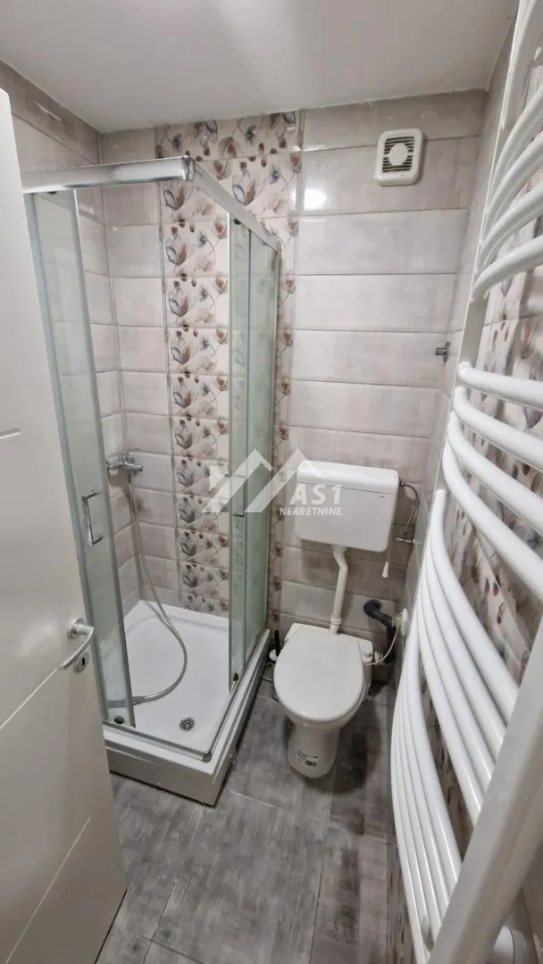 Kompaktno kupatilo sa tuš kabinom, wc šoljom i radijatorom za peškire.