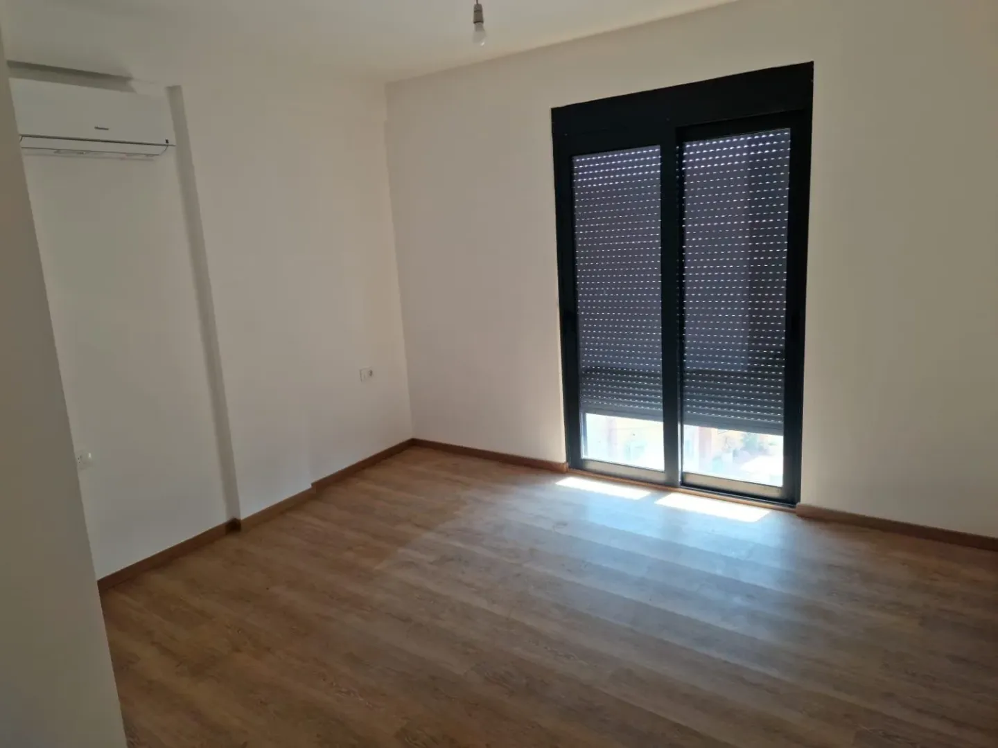 Prazna soba sa laminatom, bijelim zidovima i tamnim balkonskim vratima.