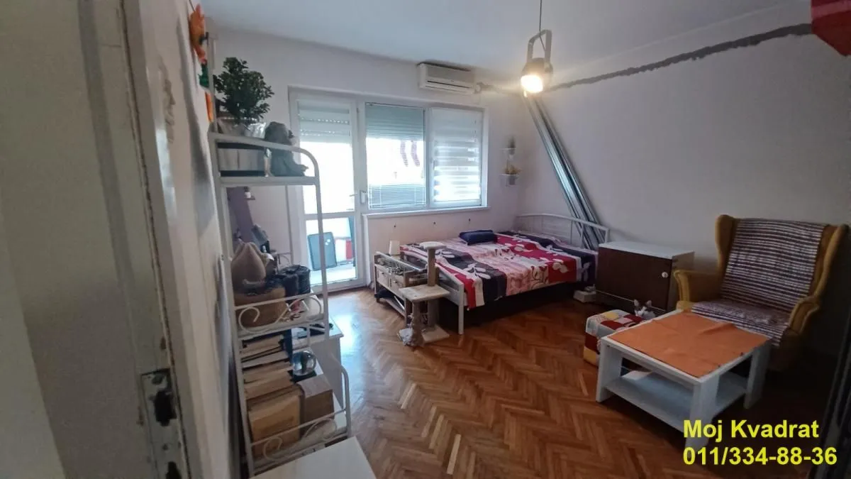 Nameštena spavaća soba sa krevetom, foteljom i izlazom na terasu.