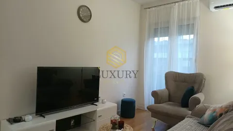Dnevna soba sa televizorom, foteljom i prozorom sa bijelim zavjesama. - image 2