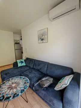 Living room with a dark blue sectional sofa, round coffee table, and air conditioning unit. - image 5