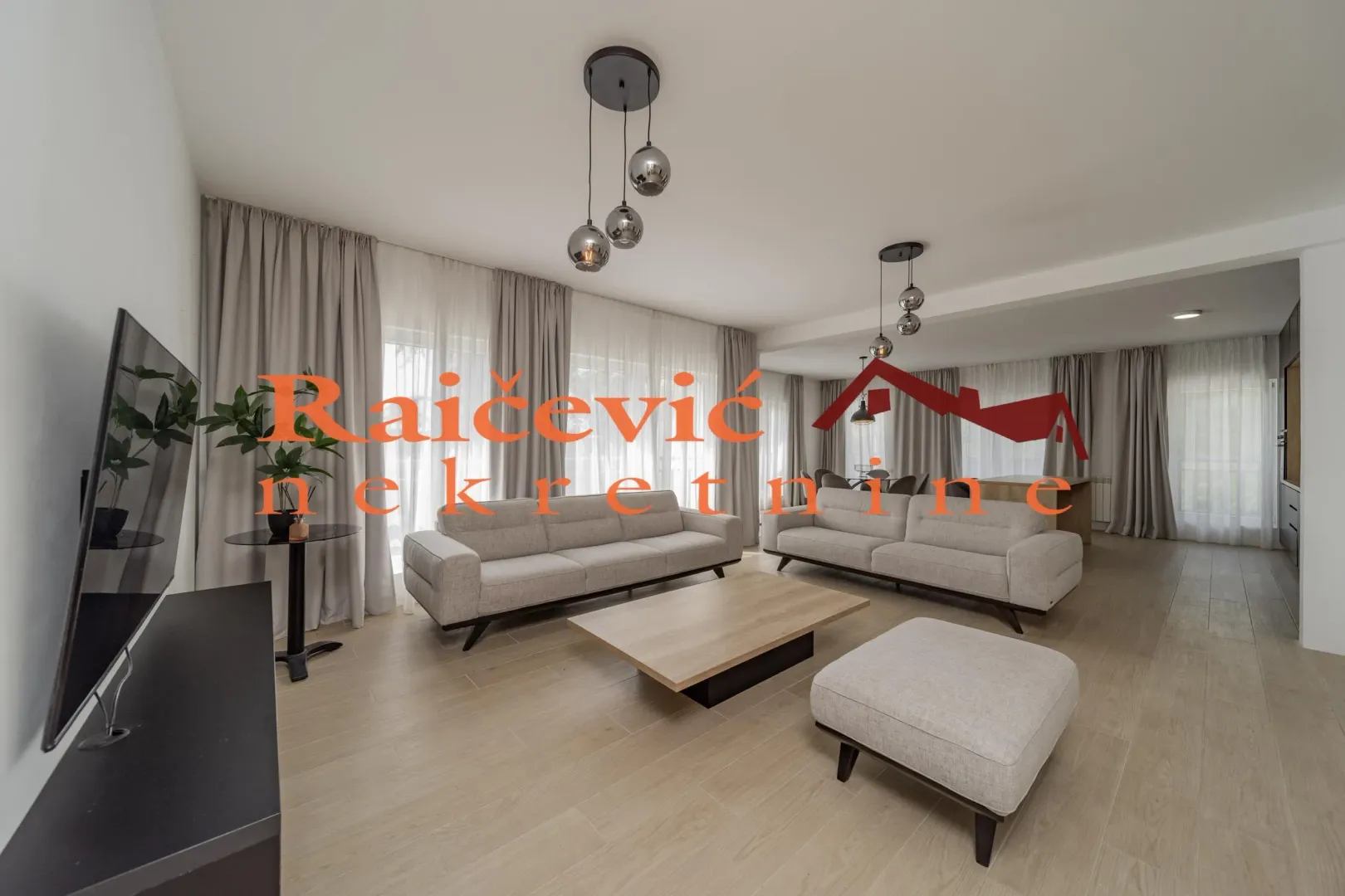Prostrani dnevni boravak sa garniturom i velikim prozorima.