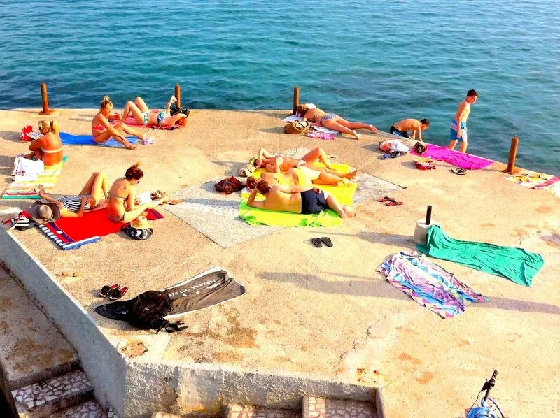 Pogled na betonsku plažu sa kupačima pored mora.
