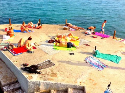 Pogled na betonsku plažu sa kupačima pored mora. - image 14
