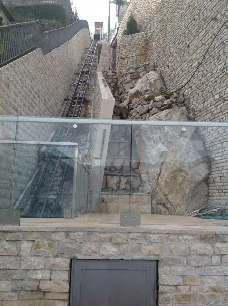 Kameni eksterijer sa kosim liftom i staklenom ogradom.