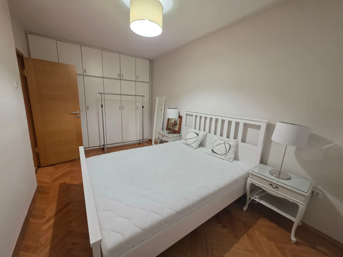 Prostrana spavaća soba sa velikim bračnim krevetom, bijelim garderoberom i parketom.