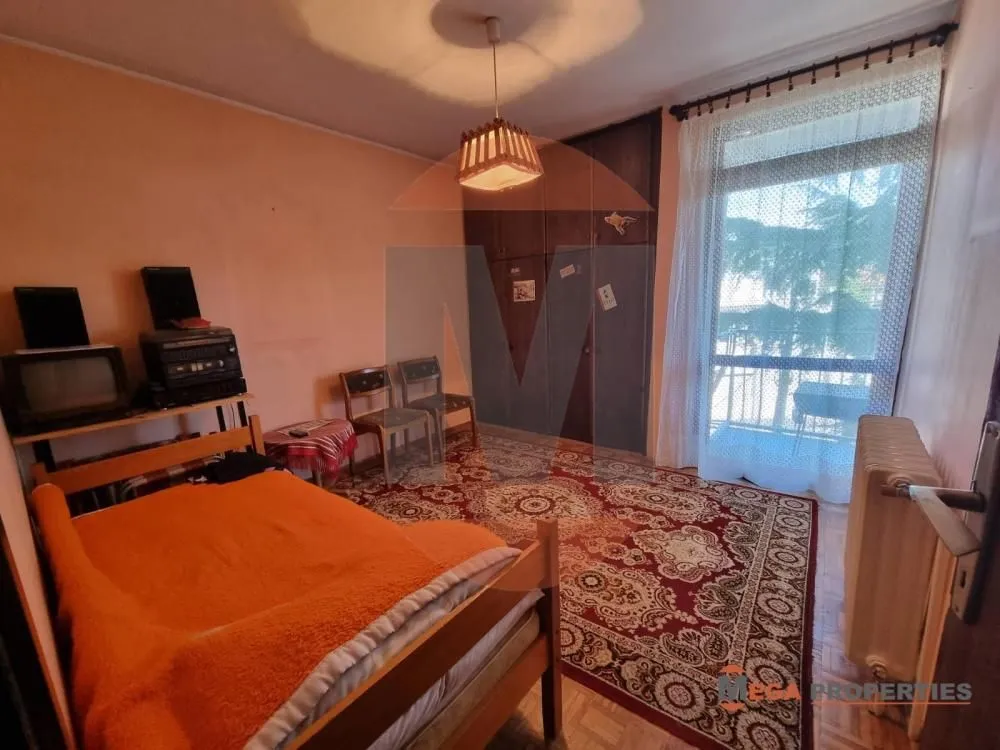 Nameštena spavaća soba sa krevetom, ormanom i izlazom na terasu.