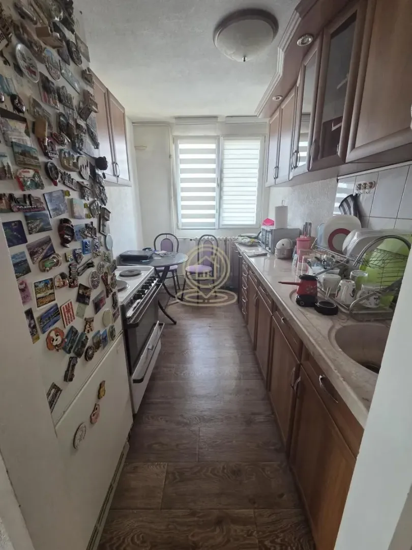 Narrow kitchen with wooden cabinetry, a refrigerator covered in magnets, and a small table at the end.