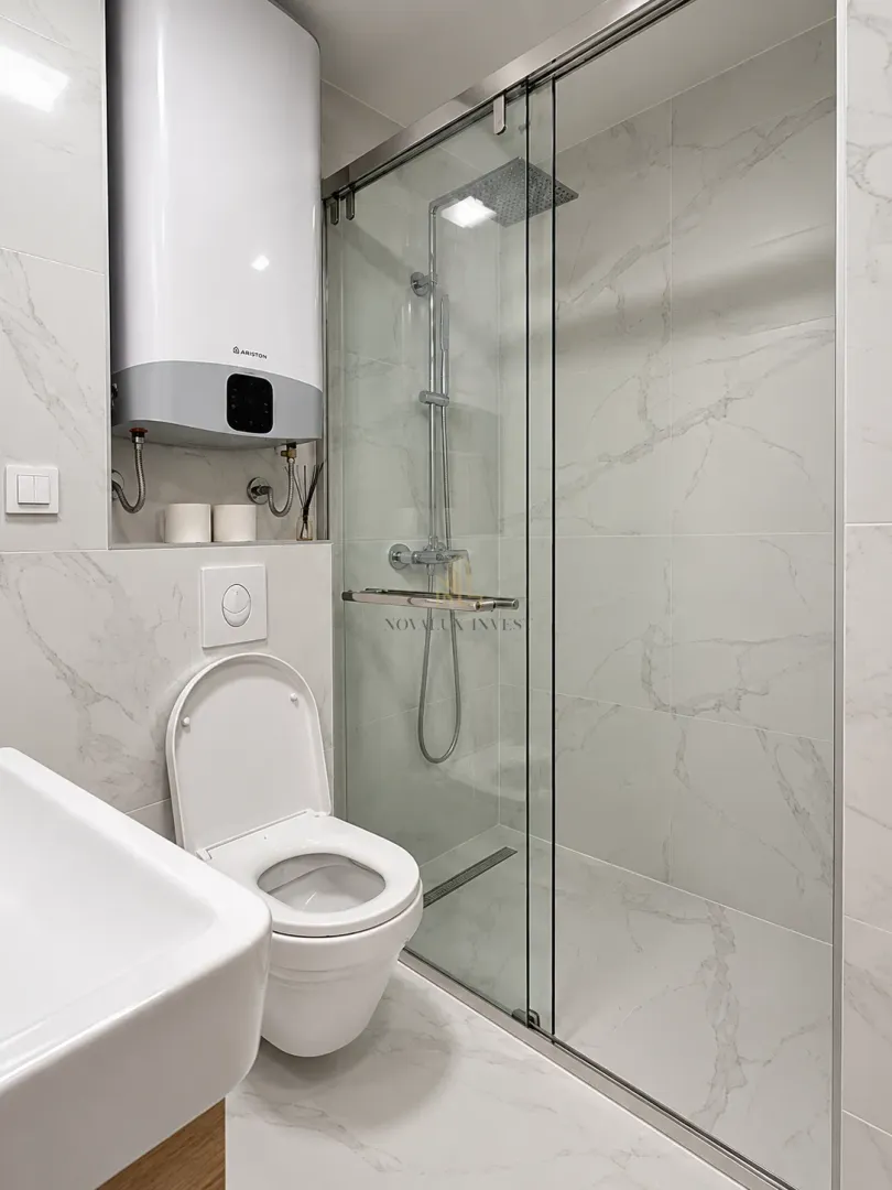 Modern bathroom with a walk-in shower, toilet bowl, and water heater on the wall.
