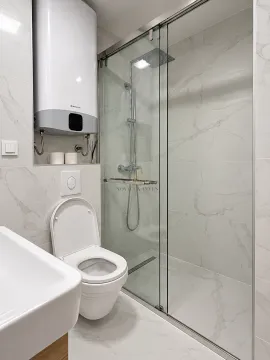 Modern bathroom with a walk-in shower, toilet bowl, and water heater on the wall. - image 10