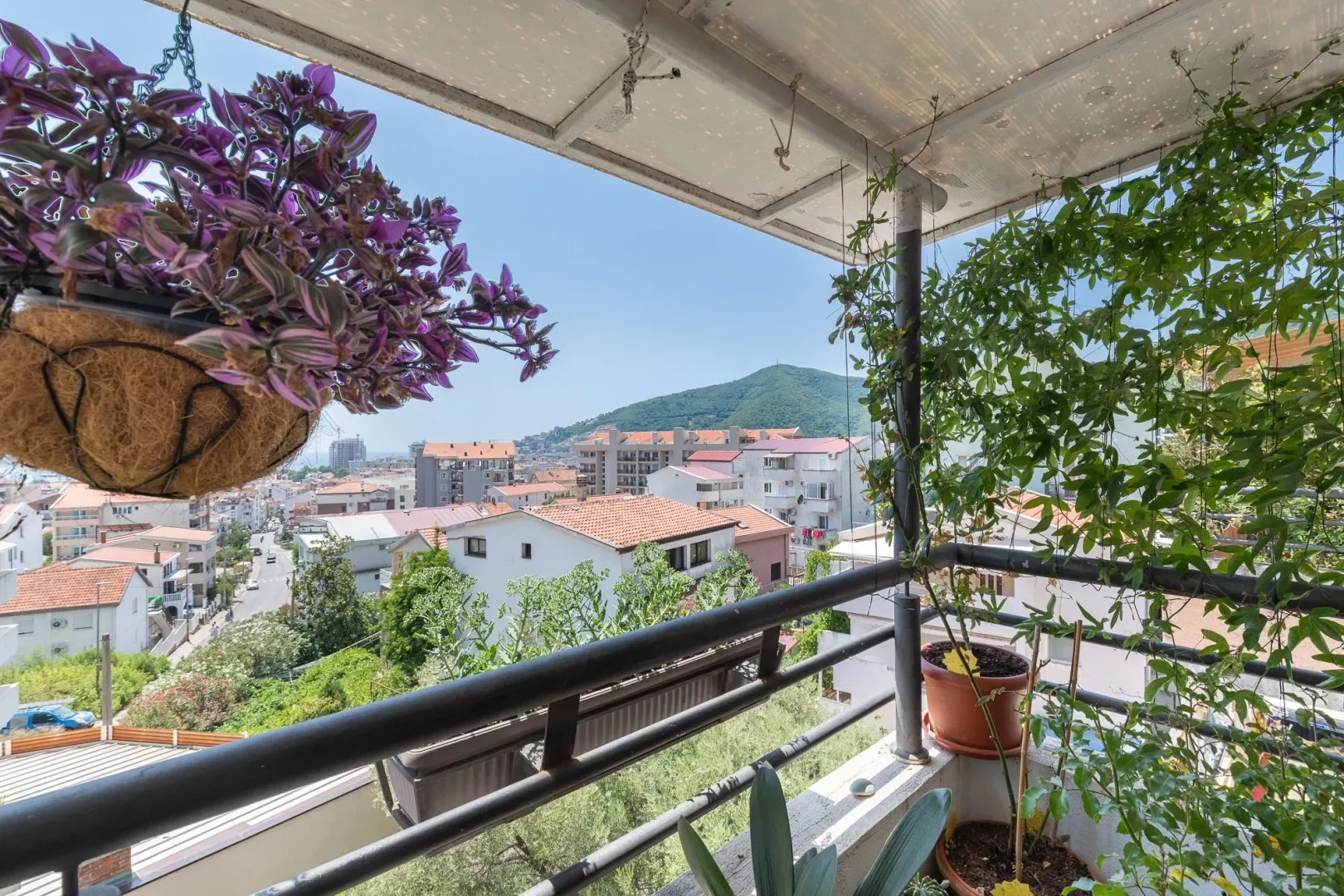 Covered balcony with flowers and a view of the city and hill.