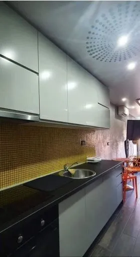 Moderna kuhinja sa bijelim elementima i tamnom radnom površinom.