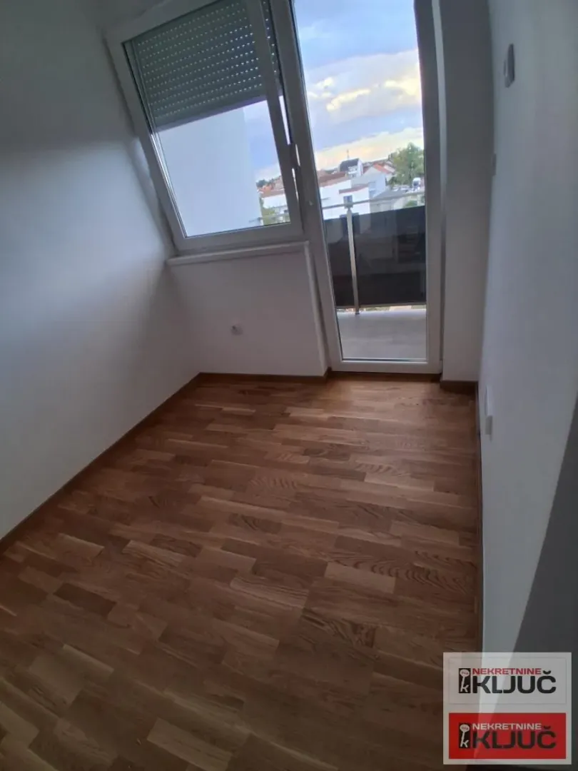 Prazna soba sa parketom i izlazom na balkon.