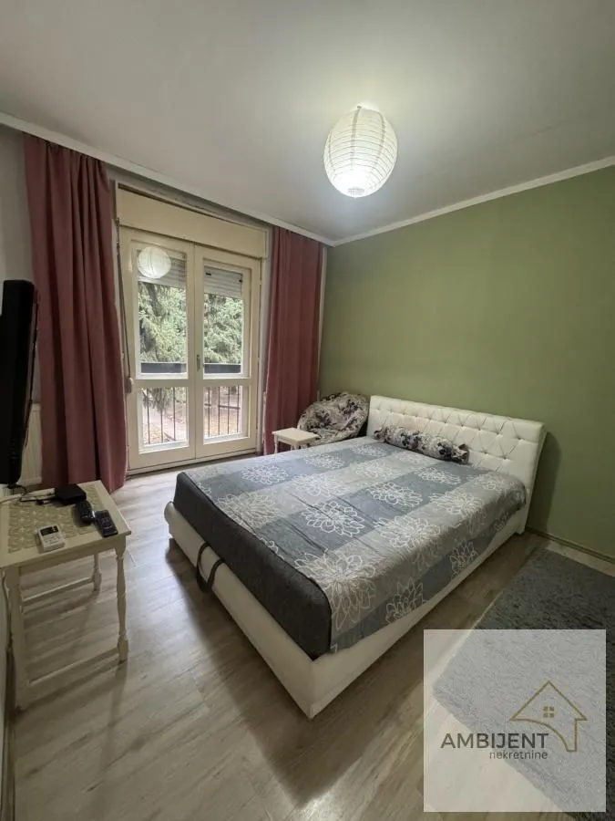Spavaća soba sa bračnim krevetom, balkonskim vratima i zelenim zidom.