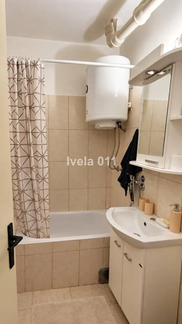 Manje kupatilo sa kadom, umivaonikom i bojlerom na zidu.