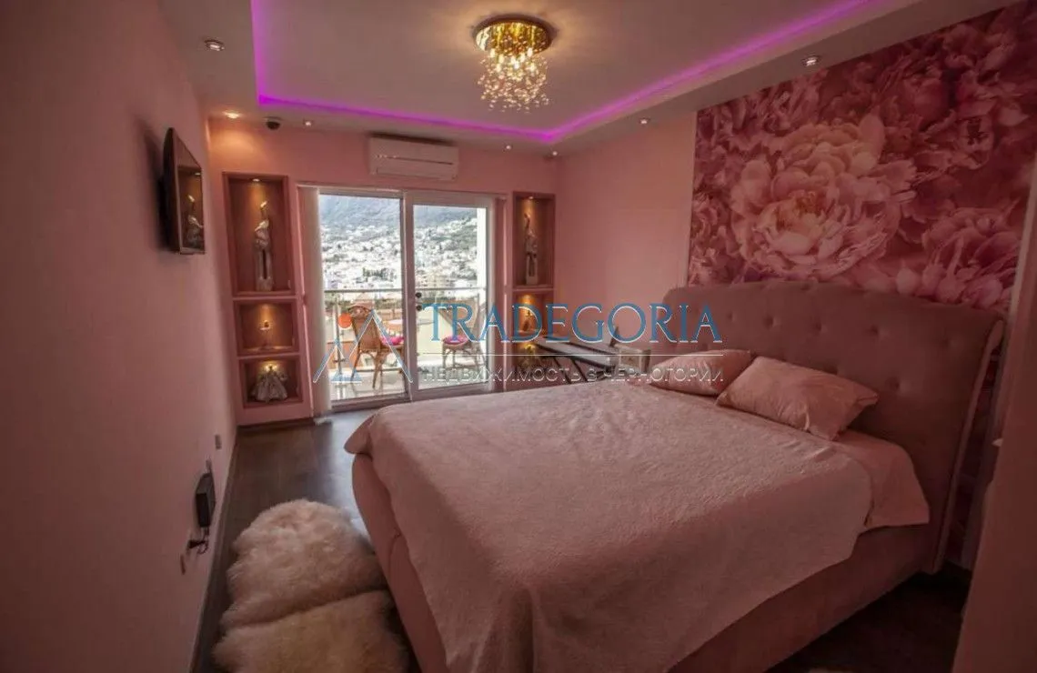 Spavaća soba sa bračnim krevetom, roze detaljima i izlazom na terasu.