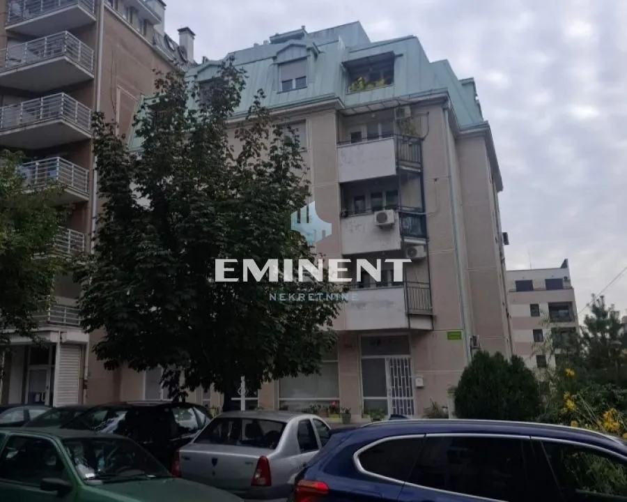 Pogled na spoljašnjost stambene zgrade sa parkiranim automobilima ispred.