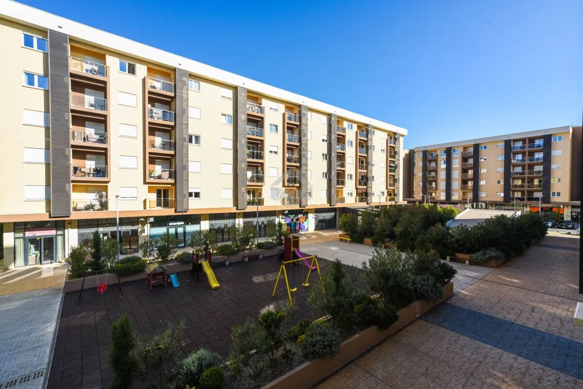 Pogled na spoljašnjost stambene zgrade sa uređenim dvorištem i igralištem.