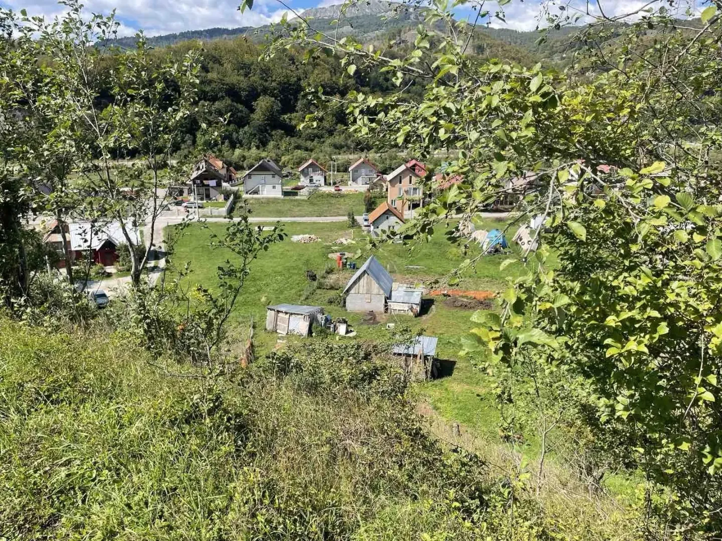 Pogled na zeleni plac sa kućama u planinskom okruženju.