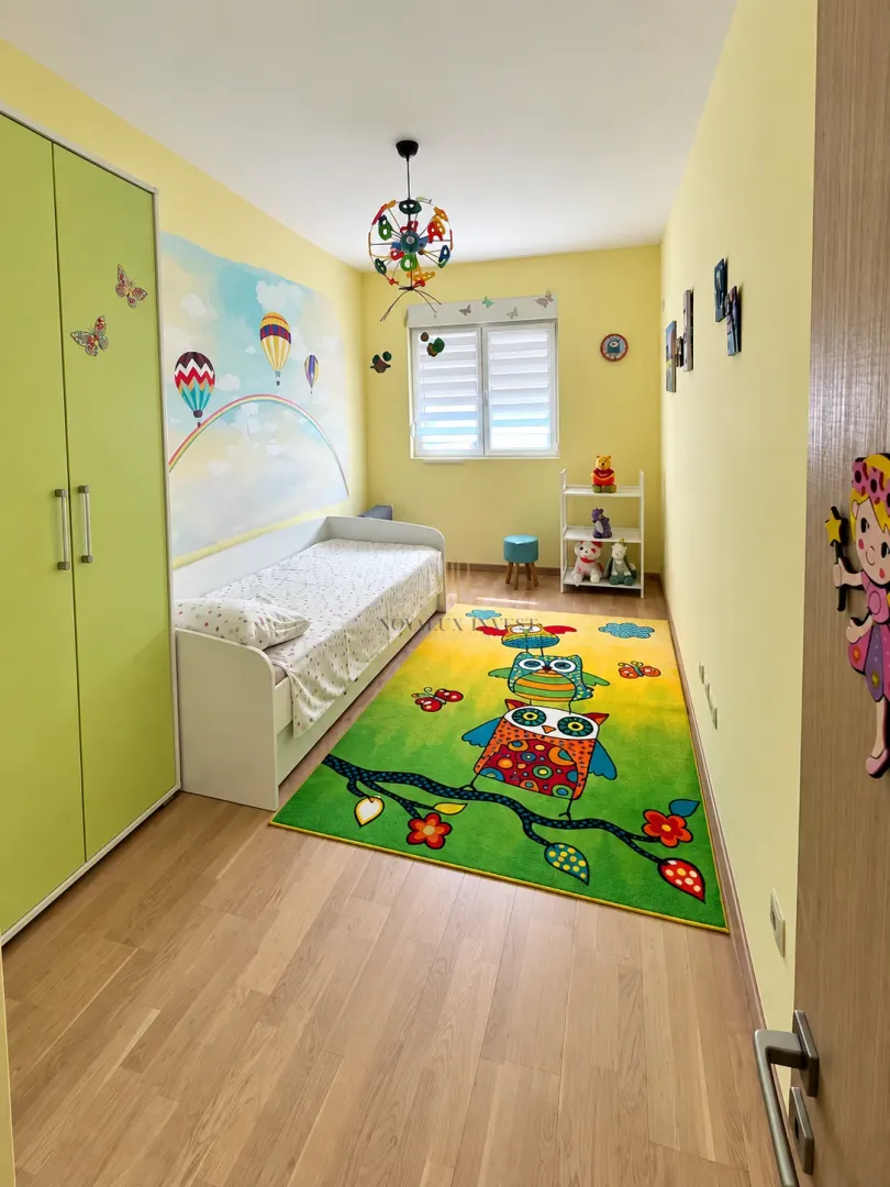 Children's bedroom with a bed, wardrobe, and colorful rug.