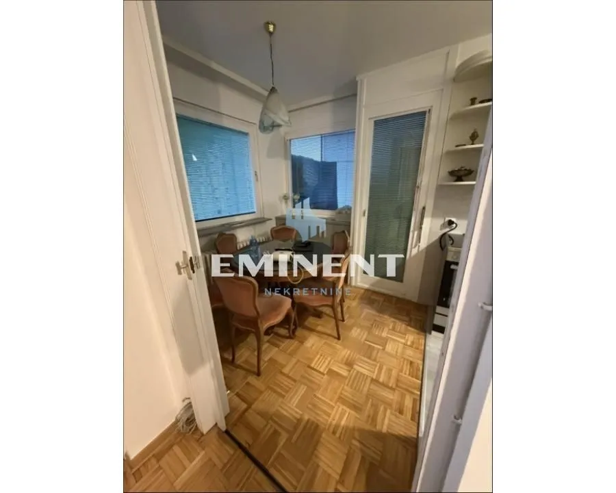 Dining area with a table and chairs, parquet flooring, and two windows.