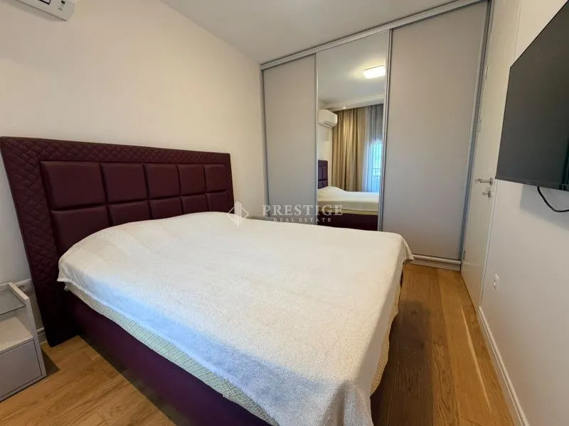Spavaća soba sa velikim bračnim krevetom, garderoberom sa ogledalom i montiranim televizorom.
