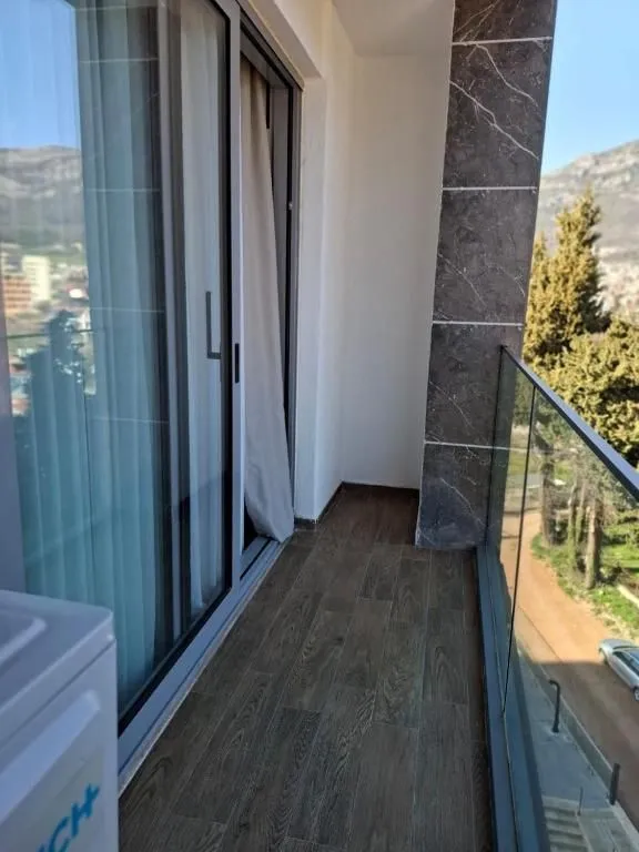Narrow tiled balcony with glass railing and surrounding view.