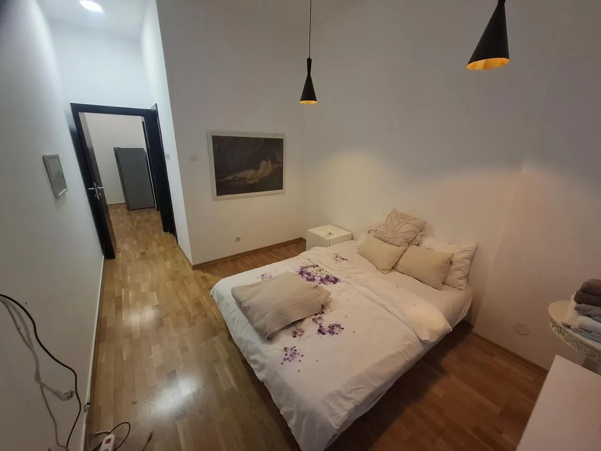 Nameštena spavaća soba sa bračnim krevetom, drvenim podom i slikom na zidu.