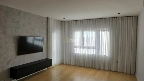 Dnevna soba sa TV-om na zidu i velikim prozorima sa belim zavesama. - image 3