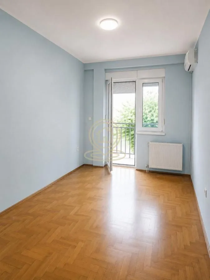 Prazna soba sa parketom i izlazom na balkon.