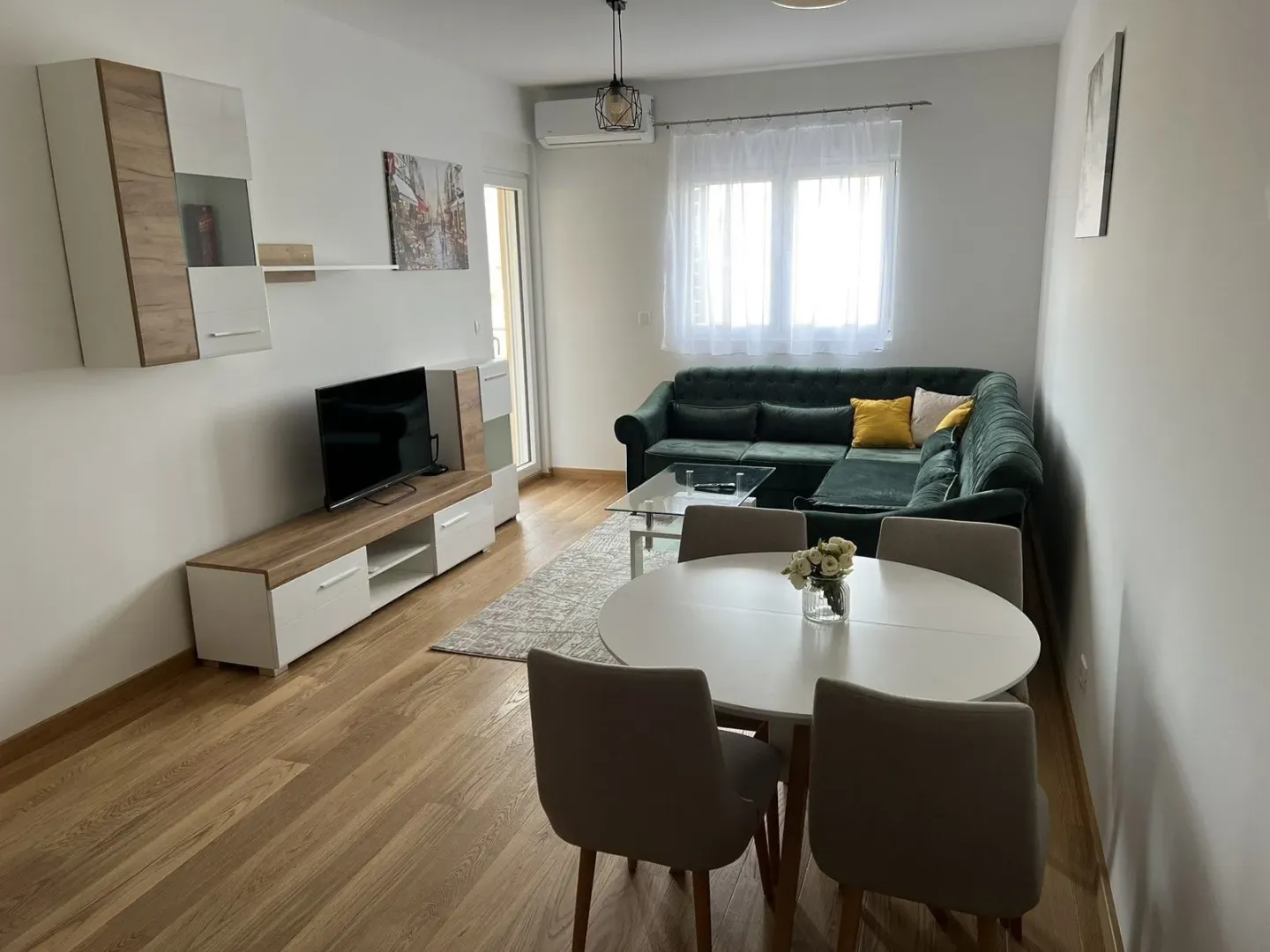 Bright living room with a green corner sofa, dining table, and TV unit.
