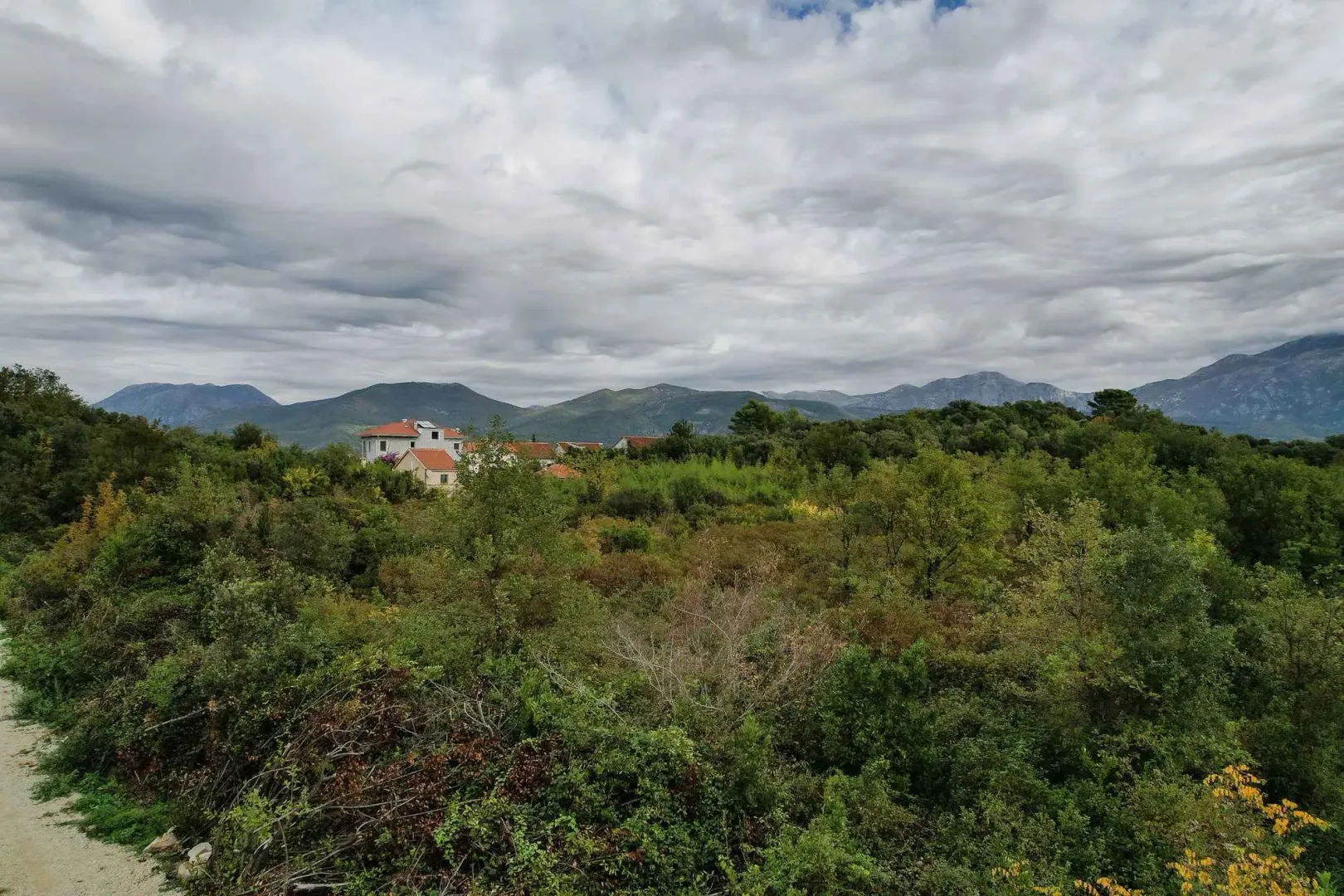 Pogled na zeleni plac i brda u daljini pod oblačnim nebom.