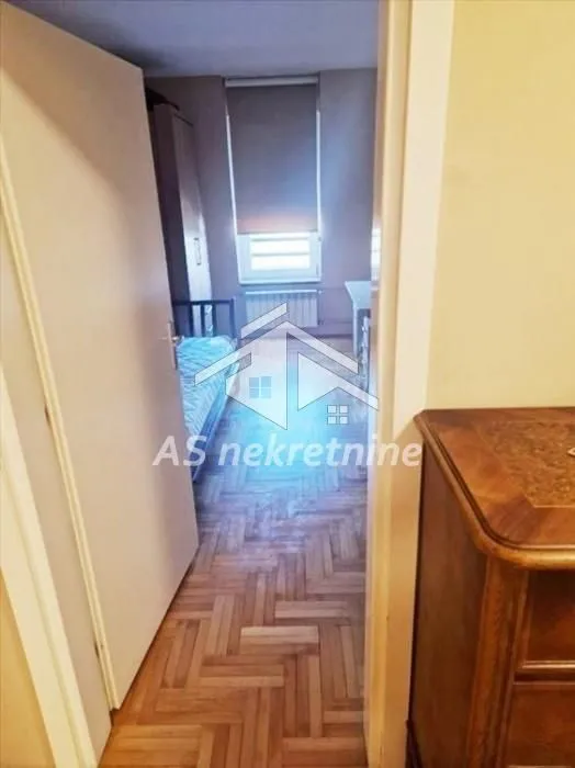 View from the hallway into a bedroom with a bed and parquet flooring.