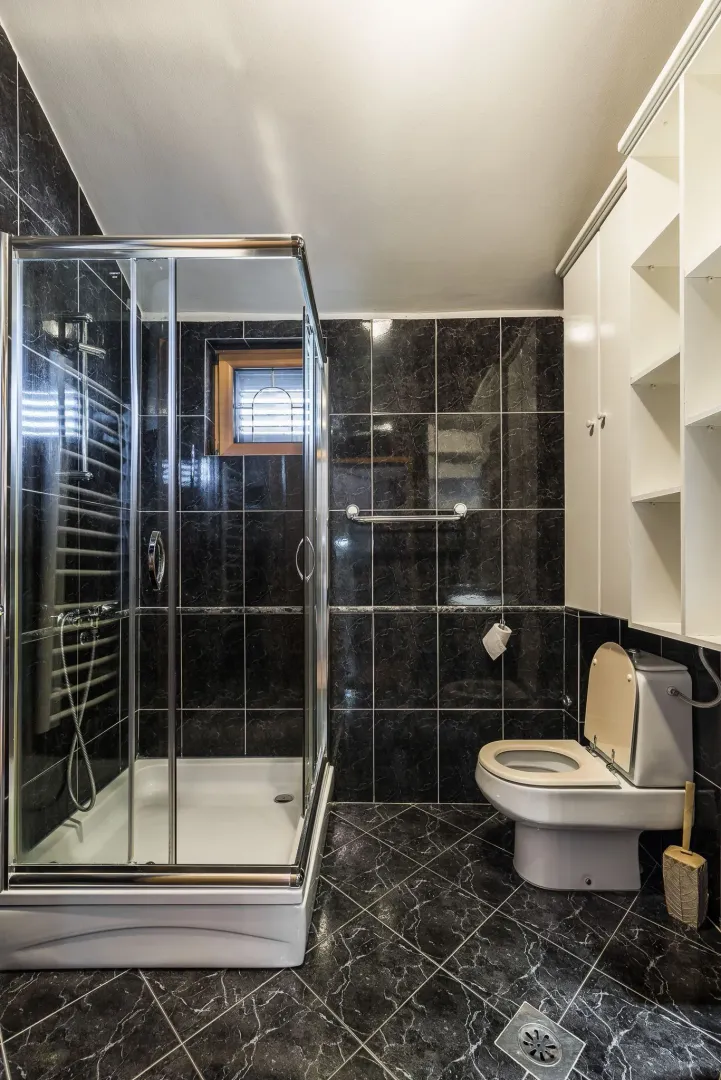 A bathroom with a shower cabin, dark tiles, and white cabinets.