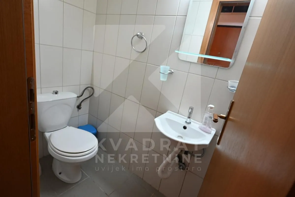 Small bathroom with white tiles, toilet, washbasin, and mirror.