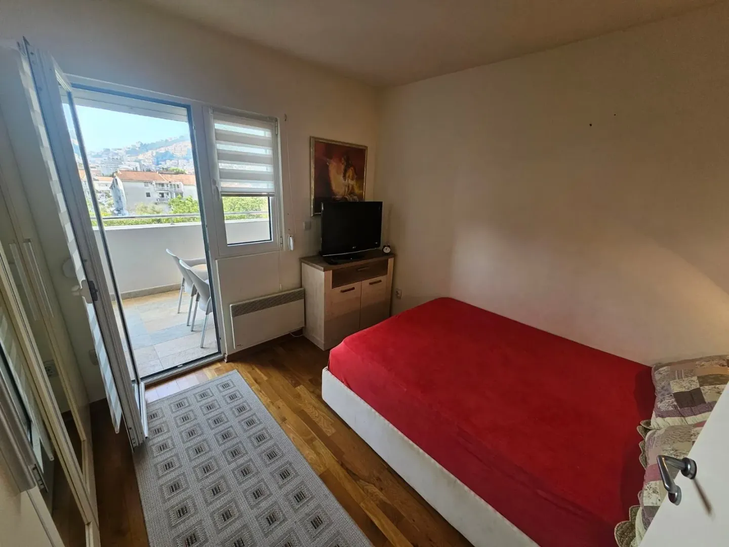 Manja spavaća soba sa krevetom, TV-om i izlazom na terasu.