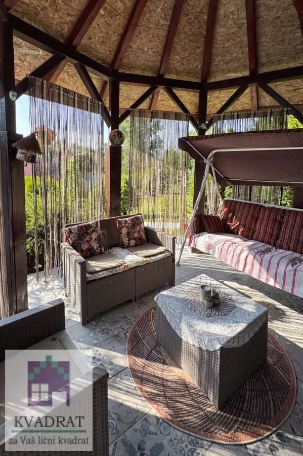 Natkrivena baštenska sjenica sa garniturom za sjedenje i ljuljaškom.
