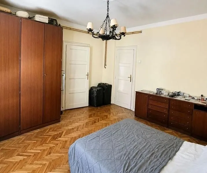 Spavaća soba sa bračnim krevetom, drvenim ormarom, komodom i parketom.